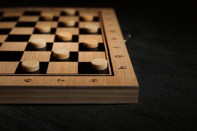 Photo of Wooden checkerboard with game pieces on black table, closeup