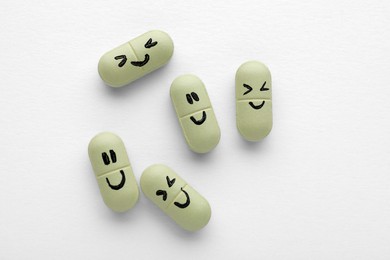 Photo of Antidepressant pills with emotional faces on white background, top view