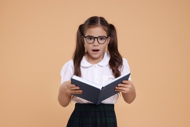 Photo of Surprised schoolgirl in glasses with book on beige background