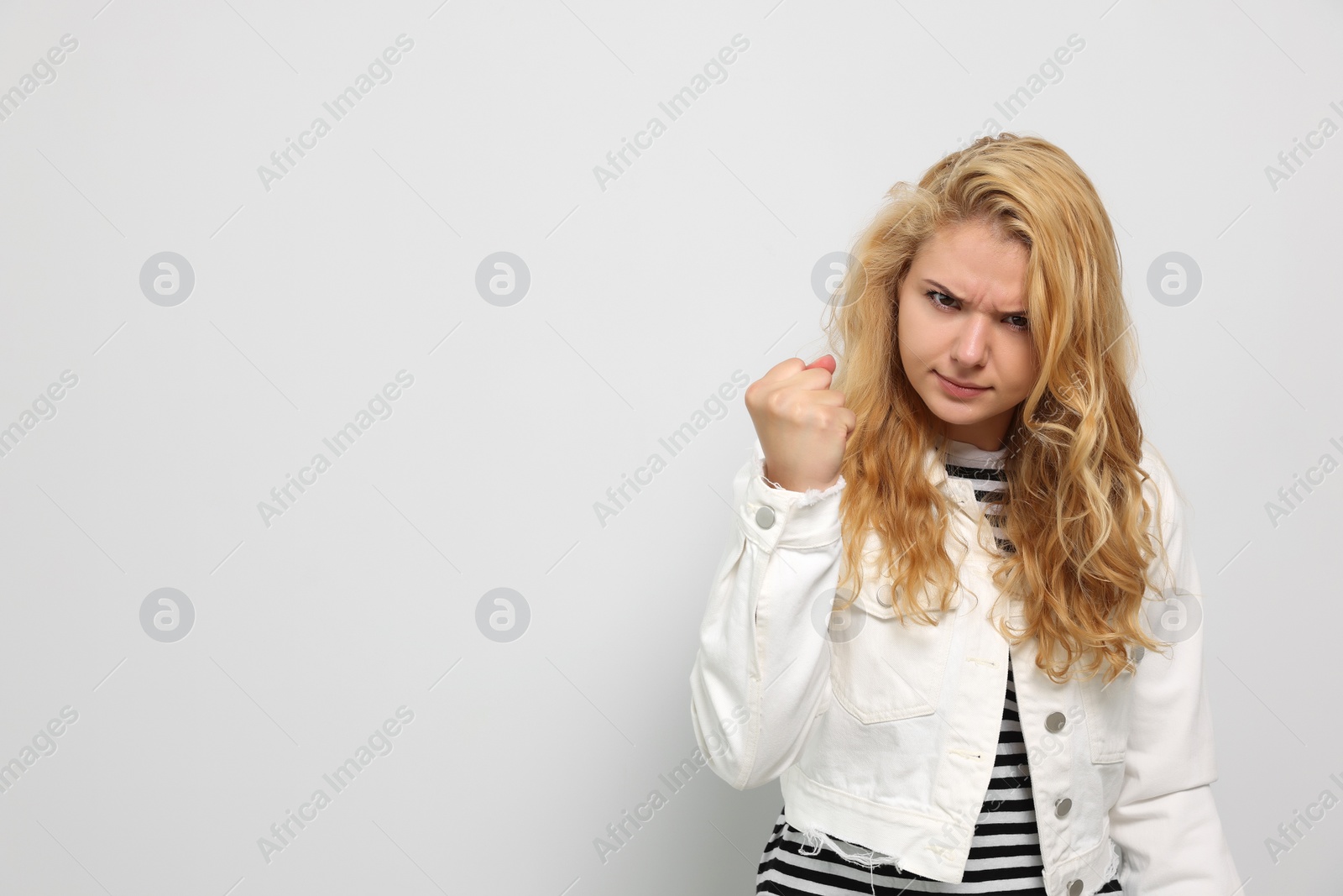 Photo of Aggressive young woman showing fist on white background. Space for text