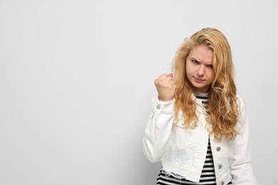 Aggressive young woman showing fist on white background. Space for text