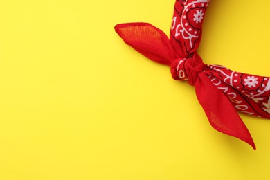 Photo of Tied red bandana with paisley pattern on yellow background, top view. Space for text