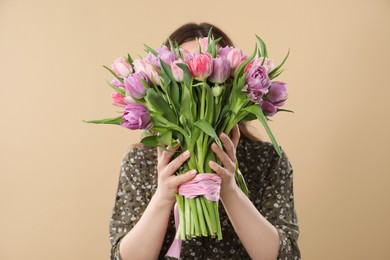 Young woman holding bouquet of beautiful tulips on beige background