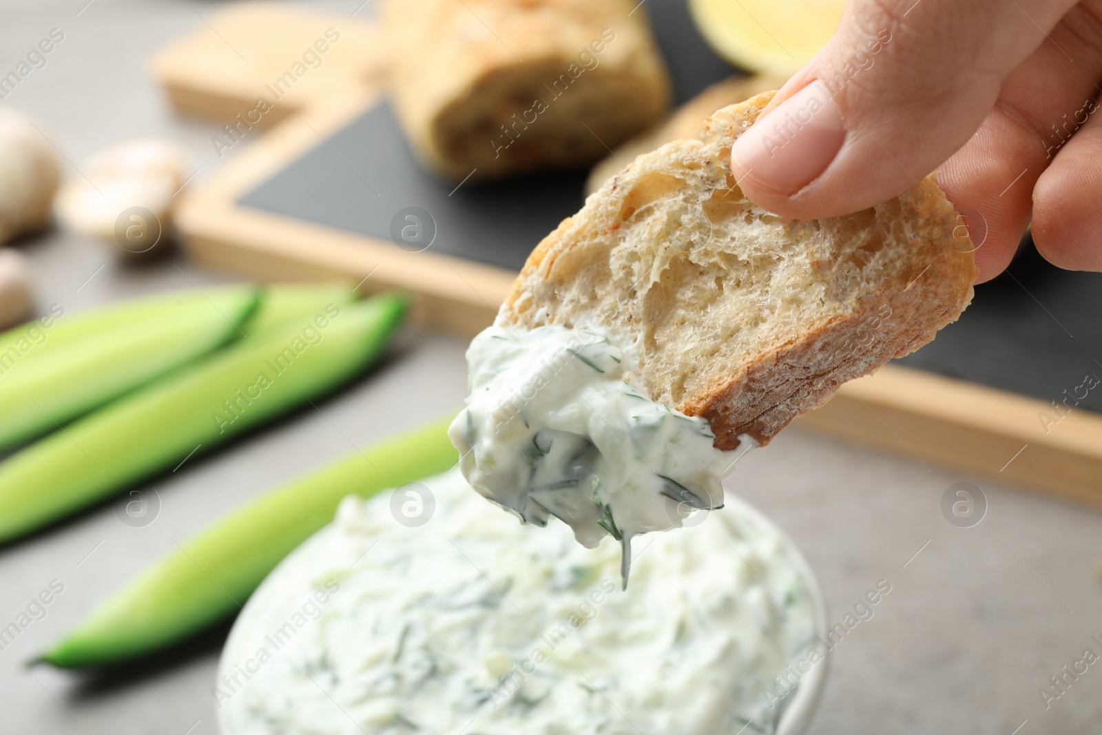 Photo of Woman dipping bread in cucumber sauce on blurred background. Traditional Tzatziki