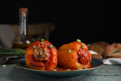 Photo of Delicious stuffed peppers served with green onion on blue wooden table against dark background, space for text