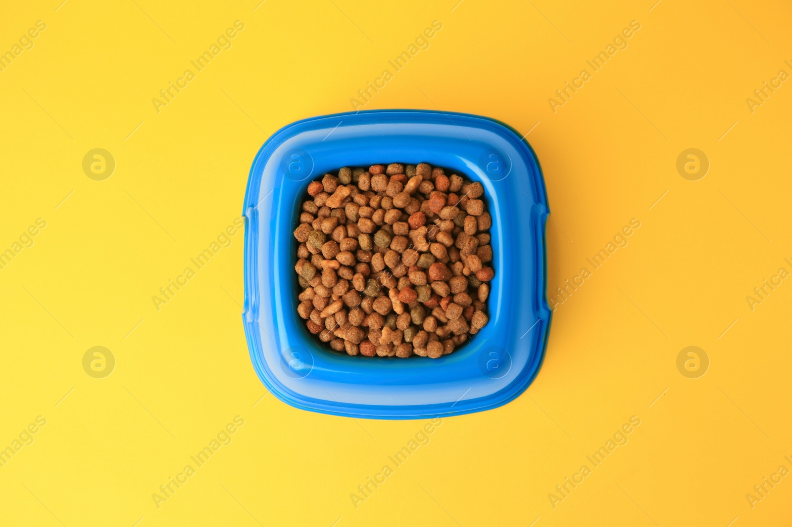 Photo of Dry pet food in feeding bowl on yellow background, top view