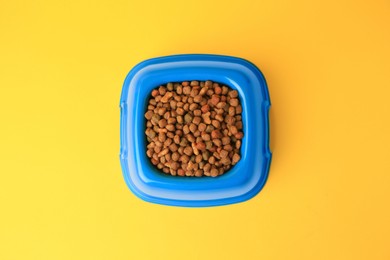 Photo of Dry pet food in feeding bowl on yellow background, top view