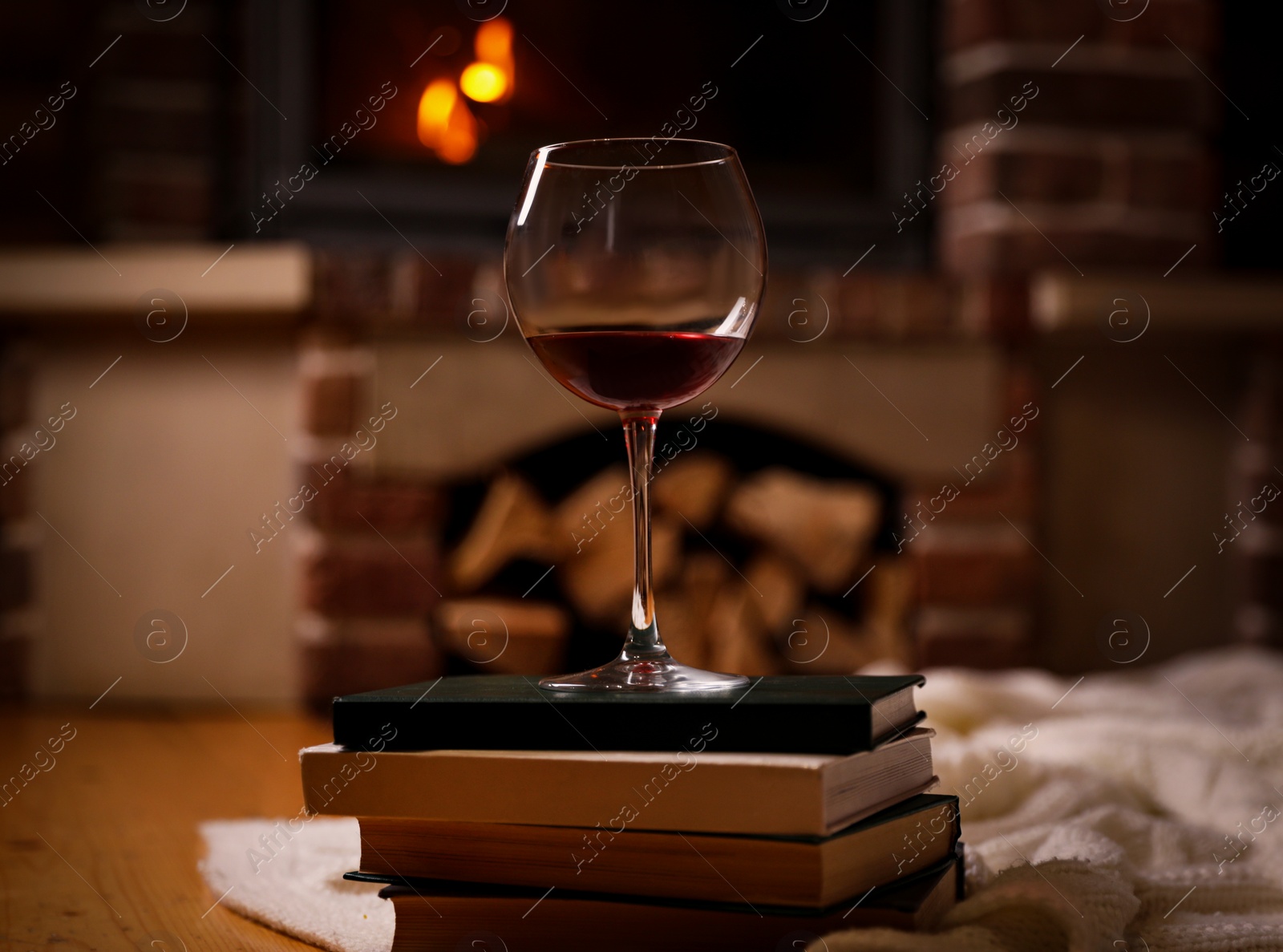 Photo of Glass of wine on books near fireplace indoors