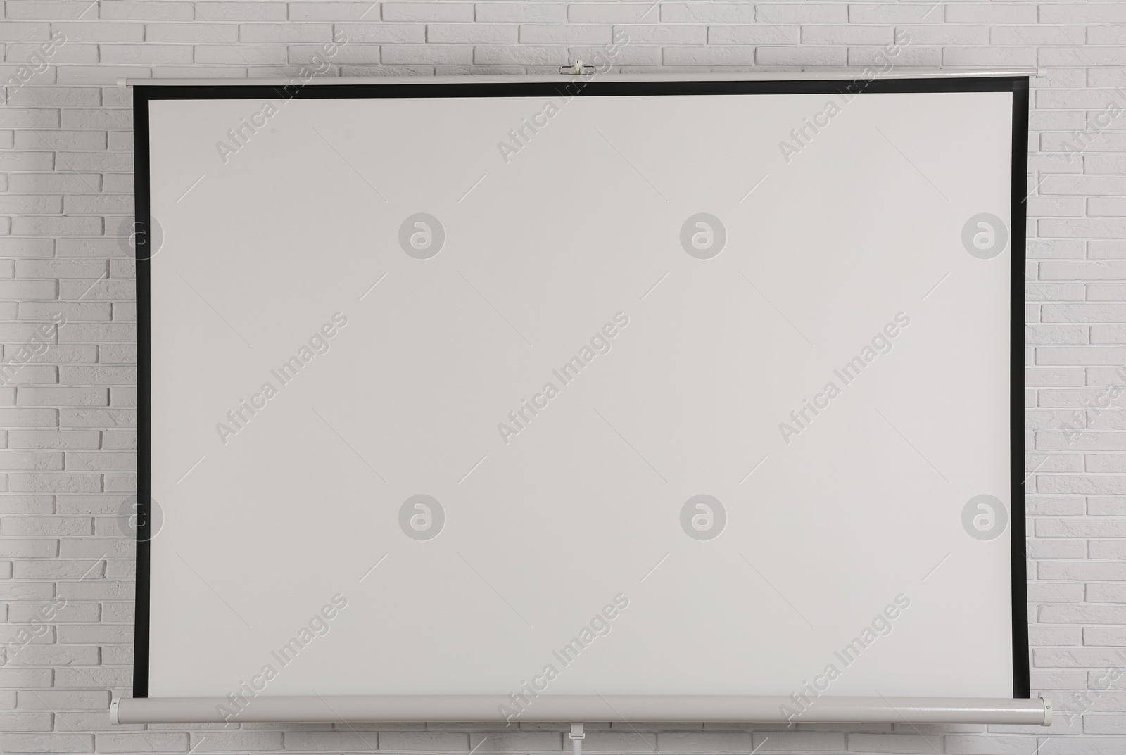 Photo of Blank projection screen near white brick wall indoors. Space for design