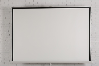 Blank projection screen near white brick wall indoors. Space for design