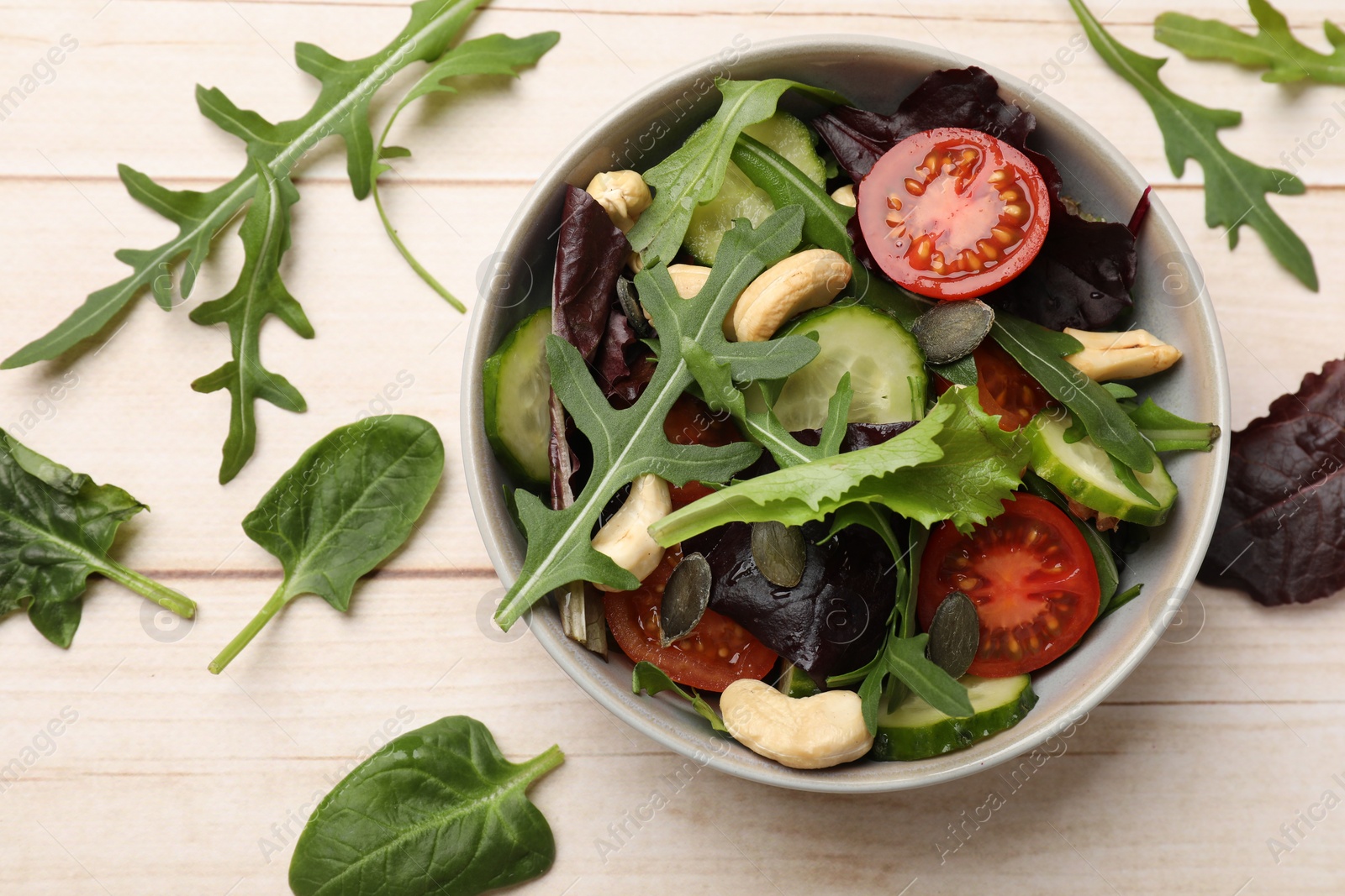 Photo of Tasty fresh vegetarian salad and ingredients on light wooden table, top view