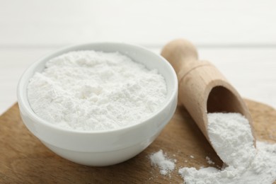 Baking powder in bowl and scoop on white wooden table, closeup