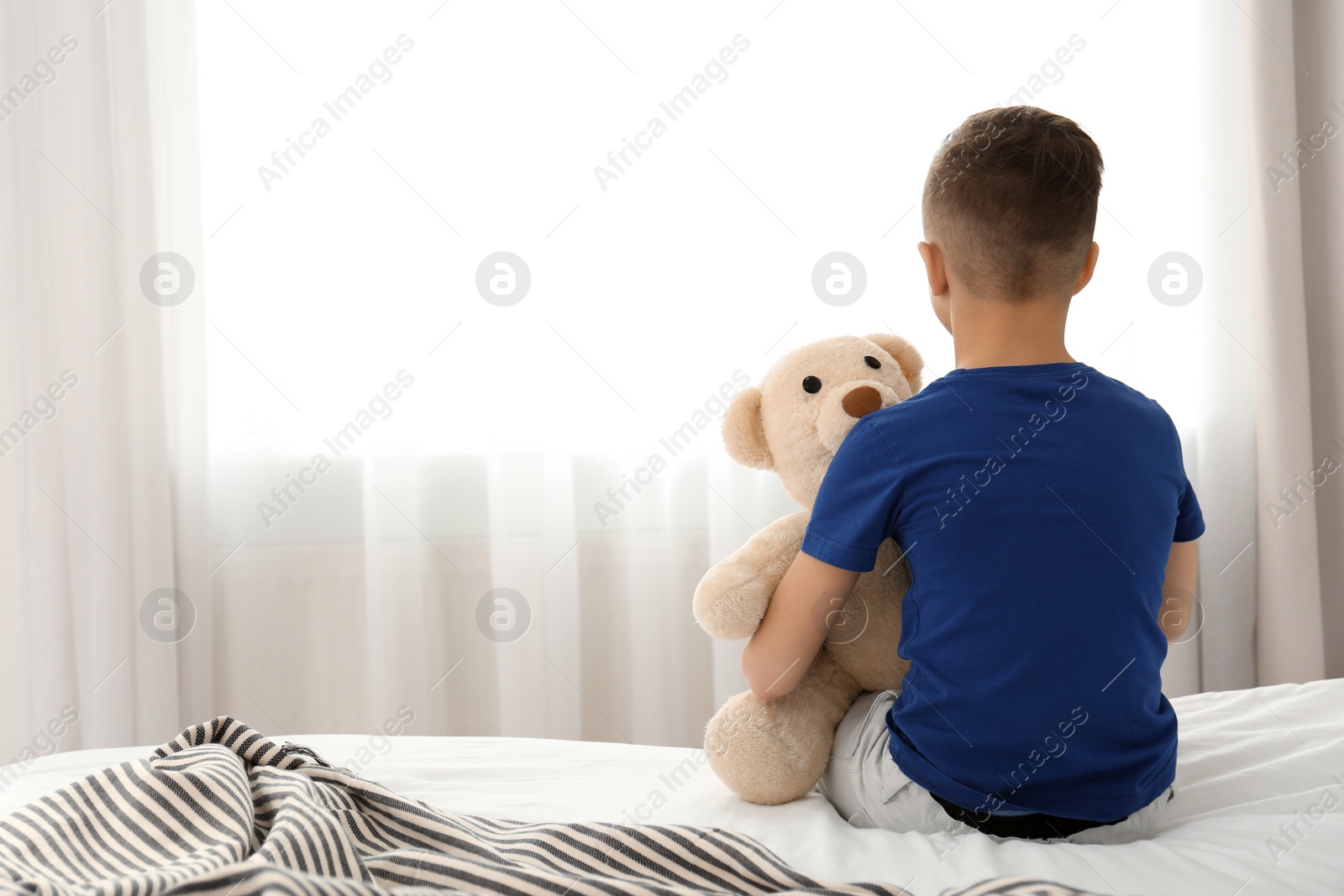 Photo of Lonely little boy sitting on bed in room. Autism concept