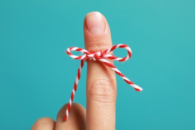 Woman showing index finger with tied bow as reminder on light blue background, closeup