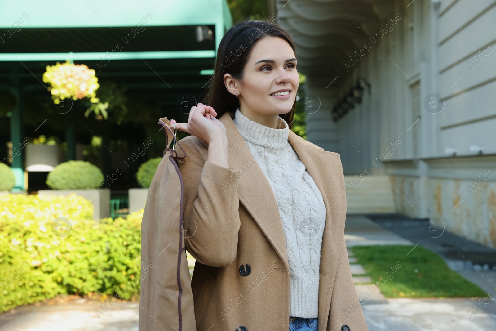 Photo of Attractive happy woman holding garment cover with clothes outdoors. Dry cleaning service