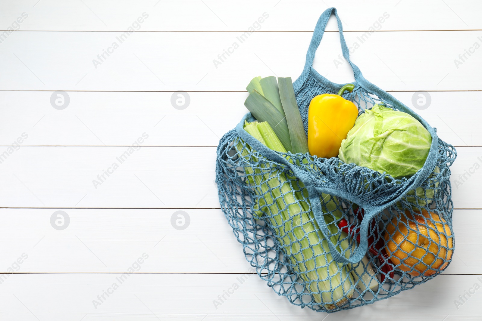 Photo of String bag with different vegetables on white wooden table, top view. Space for text