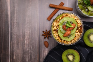 Delicious dessert with kiwi, muesli and almonds on wooden table, flat lay. Space for text