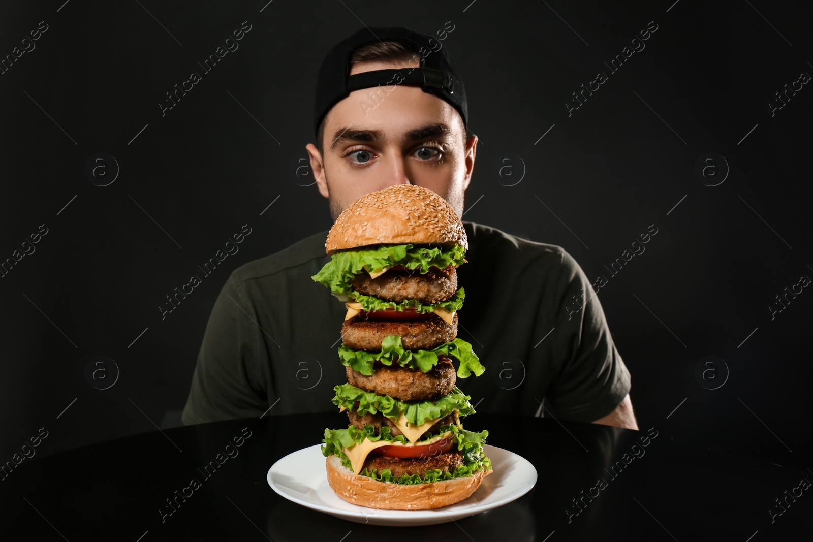 Photo of Young hungry man and huge burger on black background