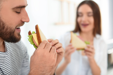 Happy couple having breakfast with sandwiches at home, closeup. Space for text