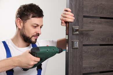 Photo of Worker with screw gun repairing door lock indoors
