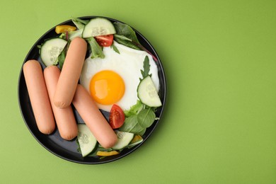 Photo of Delicious breakfast with boiled sausages and fried egg on green background, top view. Space for text