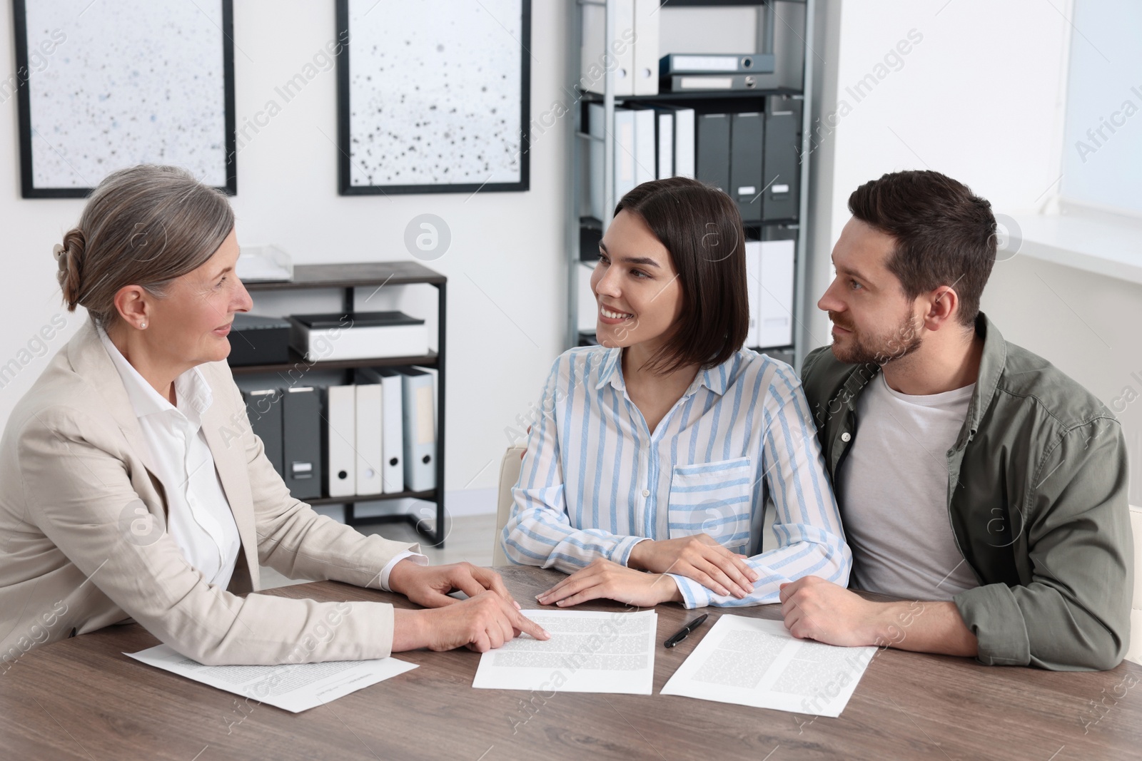 Photo of Young couple consulting insurance agent about pension plan at wooden table indoors