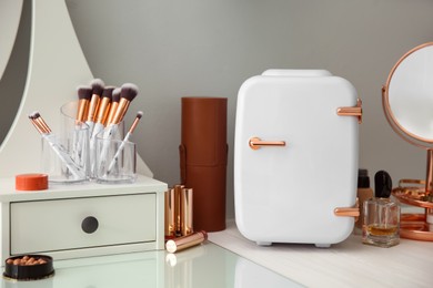 Photo of Cosmetics refrigerator and skin care products on white vanity table indoors