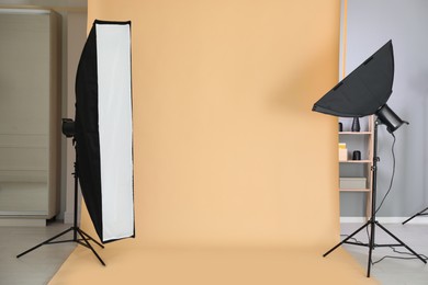 Photo of Pale orange photo background and professional lighting equipment in modern studio