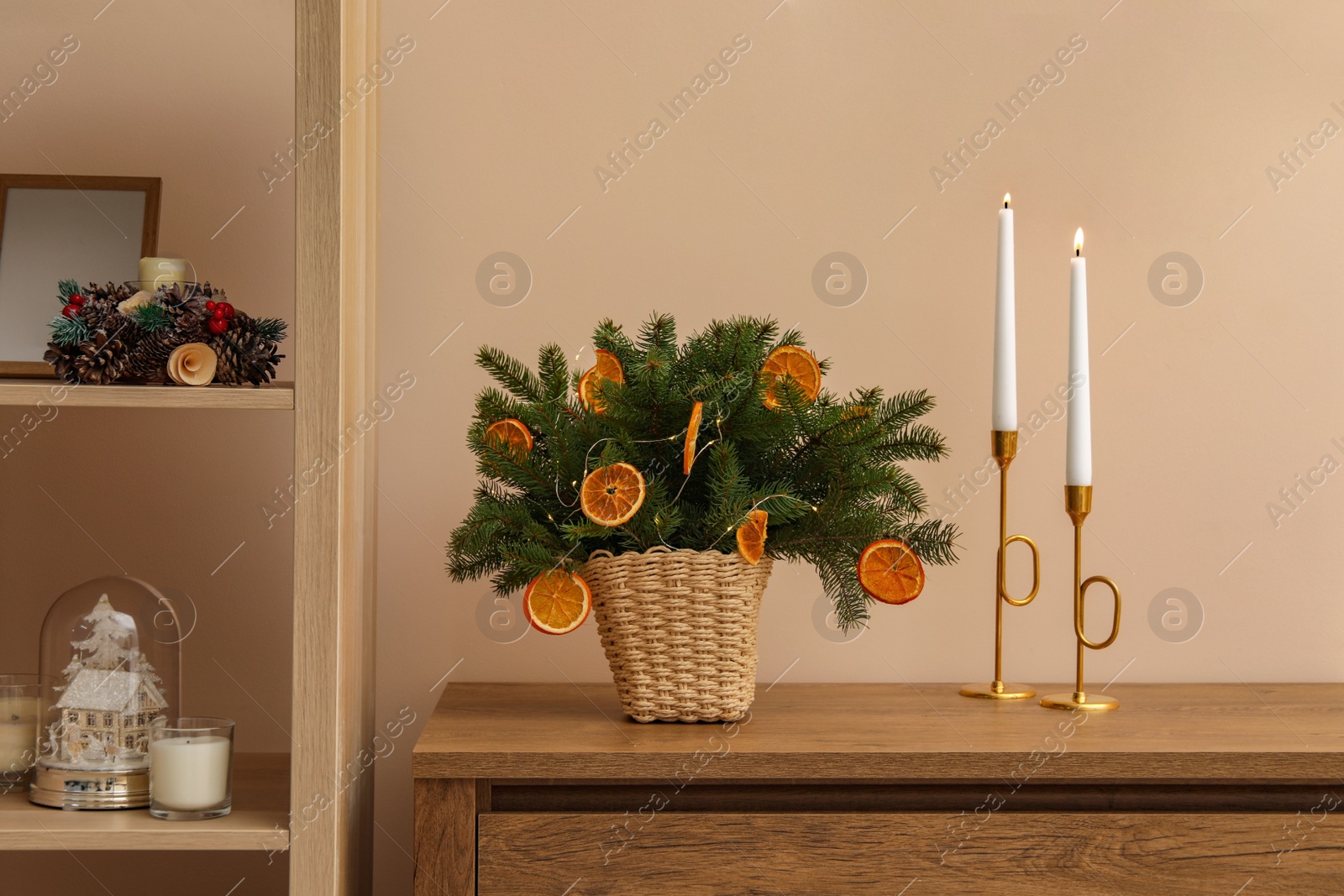 Photo of Wicker basket with fir tree branches and dried orange slices on wooden table near beige wall. Decor for stylish interior