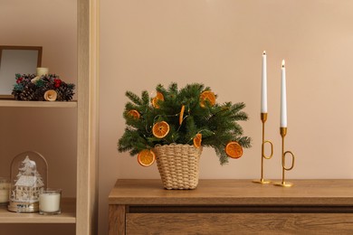 Wicker basket with fir tree branches and dried orange slices on wooden table near beige wall. Decor for stylish interior