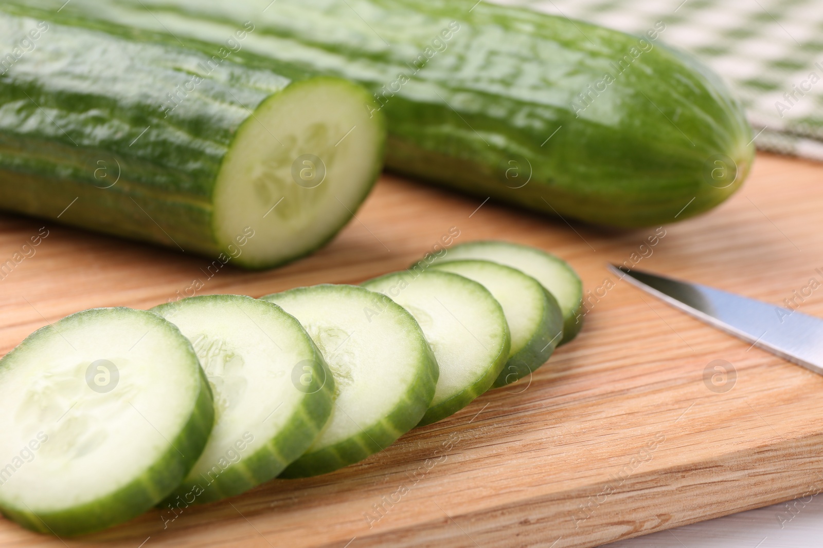 Photo of Fresh cucumbers and knife on wooden cutting board, closeup