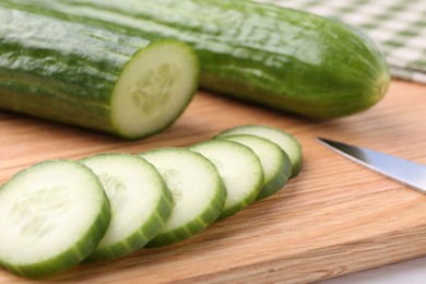 Fresh cucumbers and knife on wooden cutting board, closeup