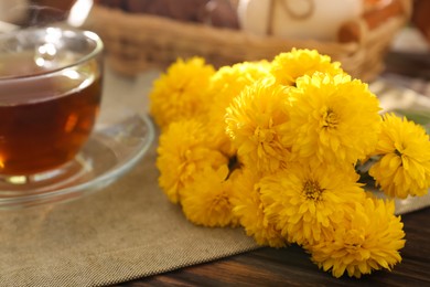 Photo of Beautiful yellow chrysanthemum flowers and cup of aromatic tea on wooden table, closeup