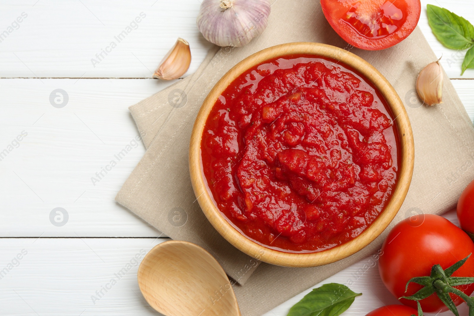 Photo of Homemade tomato sauce in bowl, spoon and fresh ingredients on white wooden table, flat lay. Space for text