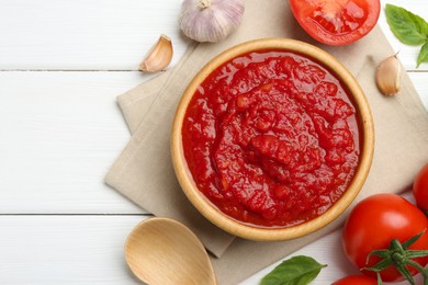 Photo of Homemade tomato sauce in bowl, spoon and fresh ingredients on white wooden table, flat lay. Space for text