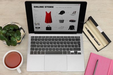 Photo of Online store. Laptop with open website, notebook, pen and pencil on wooden table, above view