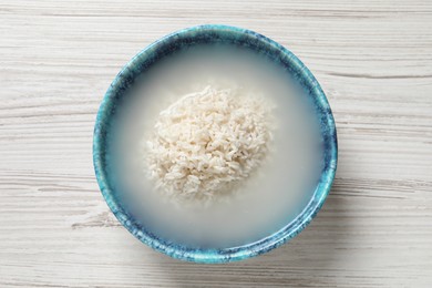 Photo of Bowl with rice soaked in water on white wooden table, top view