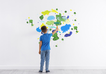 Little boy drawing on white wall indoors, back view
