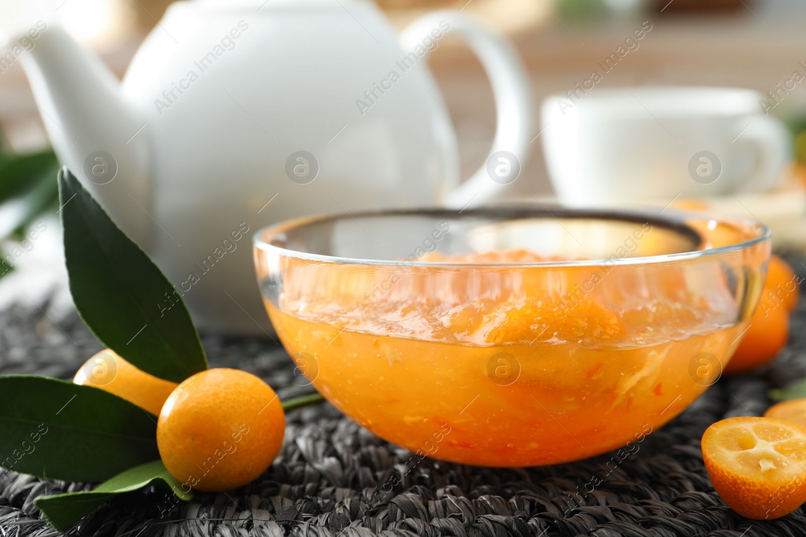 Photo of Delicious kumquat jam and fresh fruits on wicker mat, closeup