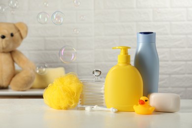 Baby cosmetic products, bath duck, sponge and cotton swabs on white table against soap bubbles