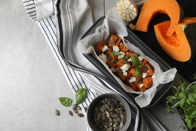 Photo of Freshly baked pumpkin pieces with cheese, seeds and basil on light table, flat lay. Space for text