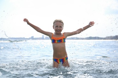 Happy little girl having fun in sea on sunny day. Beach holiday