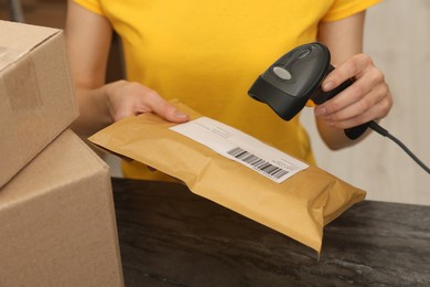 Photo of Post office worker with scanner reading parcel barcode at counter indoors, closeup