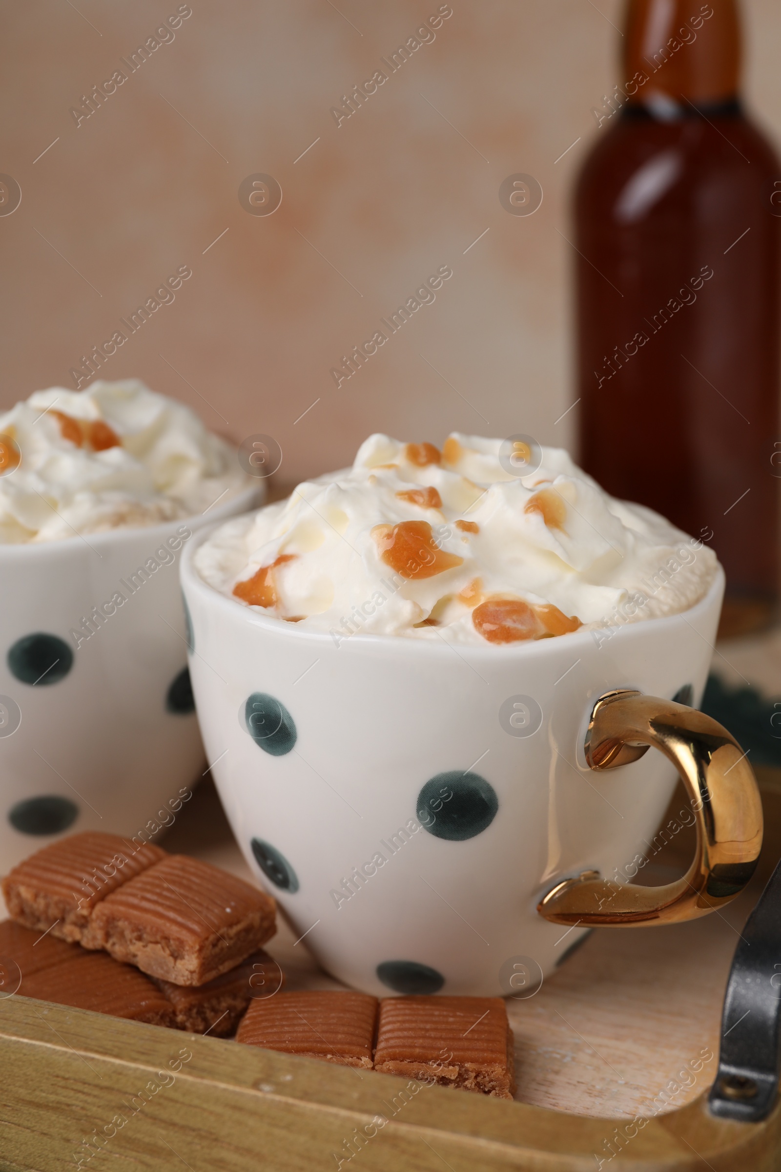 Photo of Delicious coffee with whipped cream and caramel syrup on wooden tray, closeup