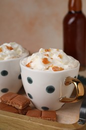 Delicious coffee with whipped cream and caramel syrup on wooden tray, closeup