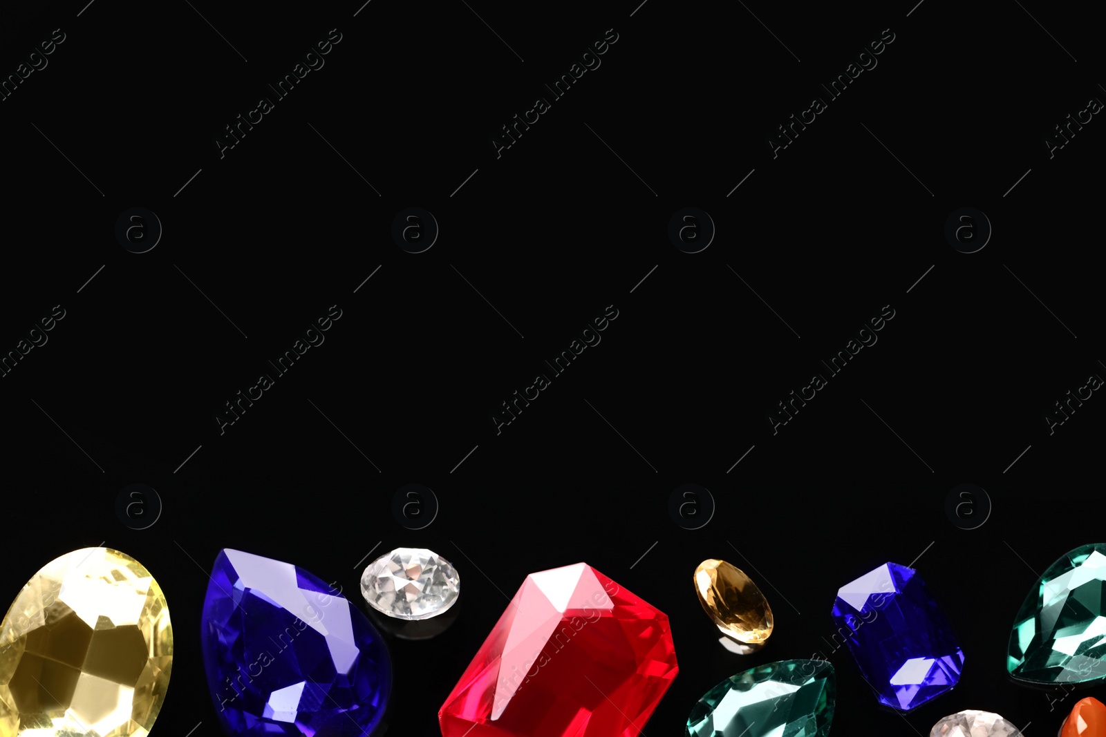 Photo of Different beautiful gemstones for jewelry on black background, flat lay. Space for text