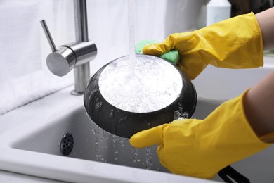 Woman washing frying pan with sponge in kitchen sink, closeup