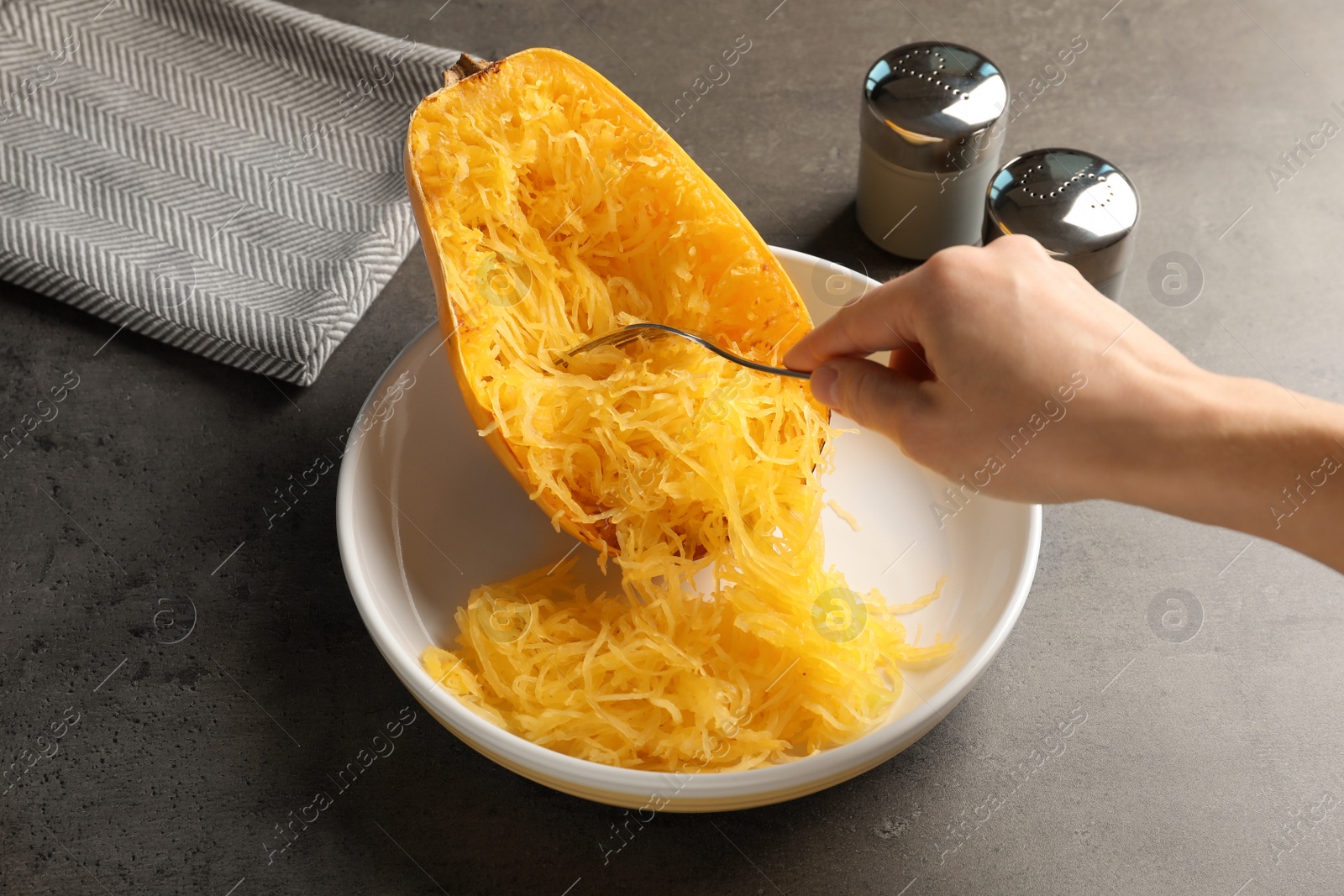 Photo of Woman scraping flesh of cooked spaghetti squash with fork at table, closeup