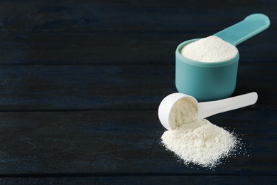 Photo of Measuring scoops of protein powder on dark wooden table. Space for text