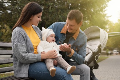 Happy parents with their adorable baby sitting on bench in park